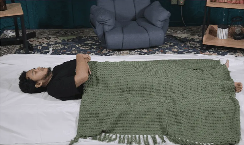 Jenazah diposisikan di atas kain kafan dengan kain penutup sementara.